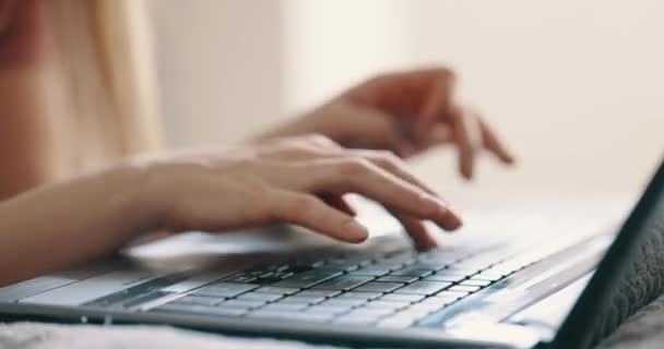 Las manos femeninas escribiendo en el teclado del ordenador portátil en la cama en el dormitorio, vista de cerca. Luz brillante y soleada — Vídeos de Stock