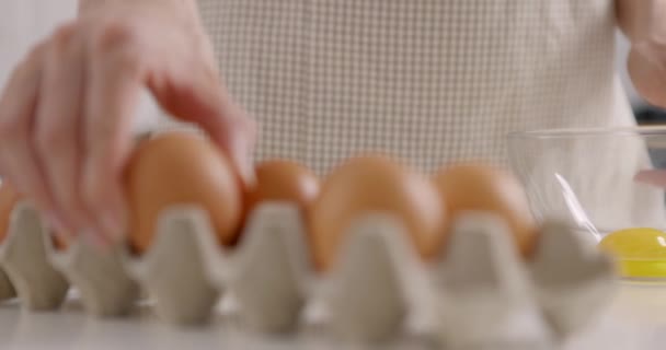 Panoramaaufnahme einer Frau in grauer Schürze nimmt das Ei aus dem Korb und zerbricht es in eine Glasschüssel. Kochen in der heimischen Küche. Zeitlupe — Stockvideo