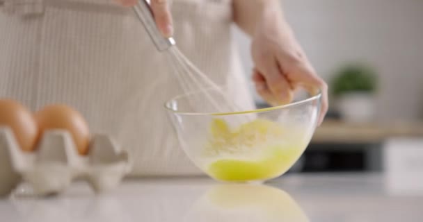 Процес змішування яєць з віночком у скляній мисці на кухні в домашніх умовах. Жінка в фартусі. Повільний рух . — стокове відео
