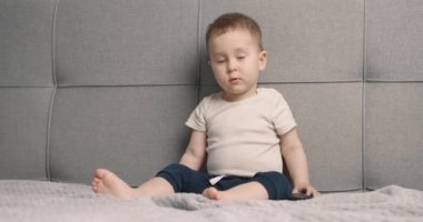 Küçük çocuk yatakta oturur ve televizyon izler. Bebek elinde uzaktan kumandayla çizgi film izliyor. Yavaş çekim.