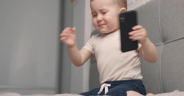 Pequeño niño enojado con un teléfono móvil en sus manos caprichos y lanza el teléfono inteligente. Movimiento lento — Vídeo de stock