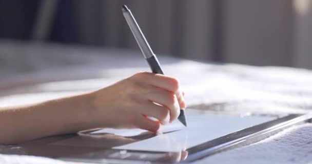 Visão de perto da mão da mulher usando o desenho do comprimido digital com caneta caneta stylus. Designer trabalhando na cama em casa. — Vídeo de Stock