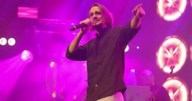 Mikrofona arka planda şarkı söyleyen bir adamın yan görüntü portresi. Havalı adam sahnede konser veriyor. Müzik ve konser konsepti.