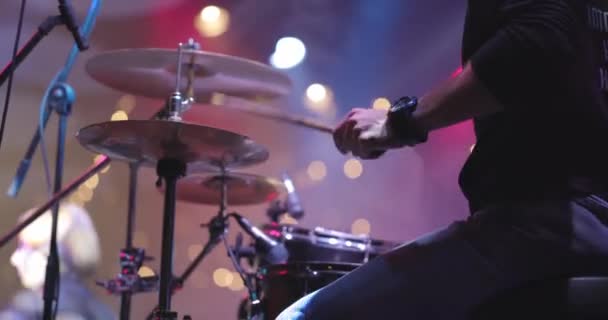 Muzikant drummer speelt muziekinstrument tegen een achtergrond van felle lichten. Live concert van popband op het podium. Sluiten van de handen — Stockvideo