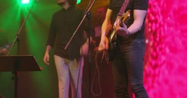 Gitarlı bir adam arka planda mikrofona şarkı söylüyor. Sahnede konser vermek. Müzik ve konser konsepti. Yavaş çekim
