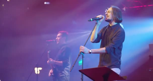 Un cantante espressivo che canta nel microfono. Concerto di musica dal vivo di fronte a luminose luci stroboscopiche colorate sul palco. Rallentatore — Video Stock