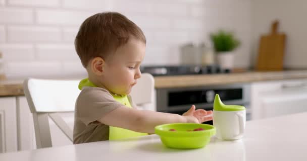 Roztomilý chlapeček jí jahody ze zeleného talíře a utírá stůl hadrem. Zpomalený pohyb. — Stock video