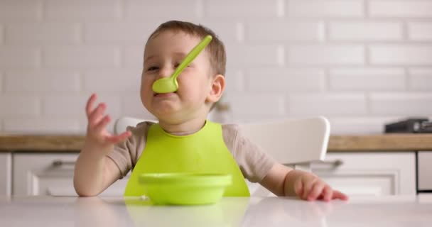 Küçük sevimli erkek bebek masada oturur ve kaşıkla oynar. Mutfaktaki mutlu çocuk kavramı. — Stok video