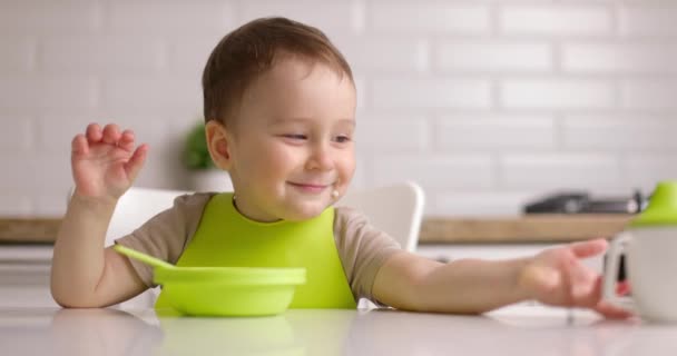 小さなかわいい笑顔の赤ちゃん男の子がテーブルに座って緑の料理で遊んでいます。コンセプト｜Happy Yildary — ストック動画