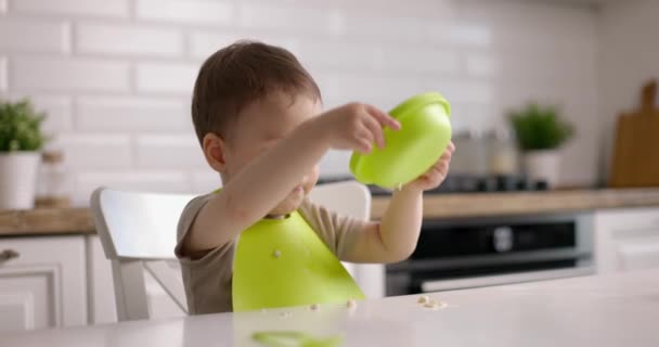 Malý roztomilý chlapeček sedí u stolu a hraje si se zelenými talíři. Koncept Happy Childhood — Stock video