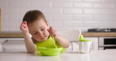 Masada oturan ve sol eliyle yulaf ezmesi yiyen küçük tatlı bir oğlan. Solak çocuk evde isteyerek yemek yiyor. Mutlu Çocukluk kavramı