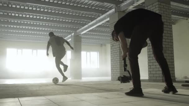 Entre bastidores. Joven hombre con electornic steadicam disparo video de entrenamiento negro chico jugador de fútbol — Vídeos de Stock