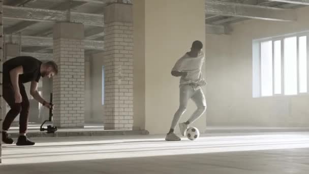 Nos bastidores. Jovem com eletornic steadicam tiro vídeo de formação jogador de futebol cara preto — Vídeo de Stock