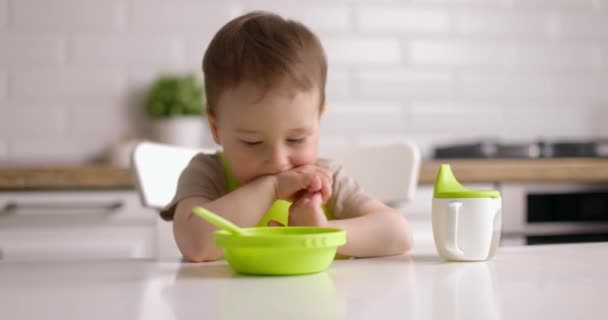 Bébé garçon mignon ne veut pas manger, agite la tête. Petit enfant assis sur une chaise à la maison cuisine. — Video