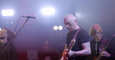 Canlı konser. Bir pop grubunun performansı, sahnede müzik grubu. Sahne ışığı ve parlak ışıklar. Vokalist, gitarist. Yavaş çekim
