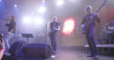 Canlı konser. Bir pop grubunun performansı, sahnede müzik grubu. Sahne ışığı ve parlak ışıklar. Vokalist, gitarist. Yavaş çekim