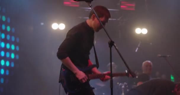 Concierto en vivo. Actuación expresiva de guitarristas en el escenario. El tipo toca la guitarra eléctrica con la luz brillante de los focos. Movimiento lento — Vídeo de stock