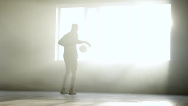 Joven negro entrena con una pelota de fútbol en el interior. Luz solar brillante en el fondo — Vídeos de Stock