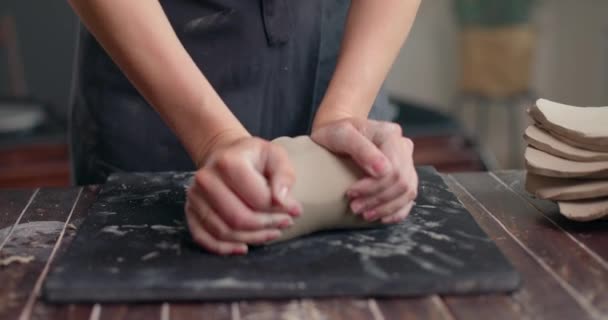 Γυναίκα γλύπτρια ζυμώνει πηλό με τα χέρια της για να δημιουργήσει κεραμικά στο εργαστήριό της. Ο καλλιτέχνης ζυμώνει πηλό για μόντελινγκ. Κοντινό πλάνο, αργή κίνηση — Αρχείο Βίντεο