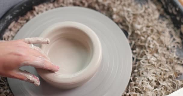 Conceito de cerâmica artesanal. Close-up de mãos de mulheres em estúdio de cerâmica. Corta a peça da roda de cerâmica. Vista superior. Movimento lento — Vídeo de Stock