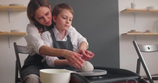 美丽的年轻母亲和可爱的男婴在工作室学习陶瓷轮上的陶器。手工陶瓷作坊。慢动作 — 图库视频影像