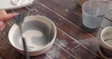 Çömlek sanatçısı çömlek atölyesinde seramik çömleği fırçayla dekore ediyor. Boya lekeleri. Yavaş çekim. 