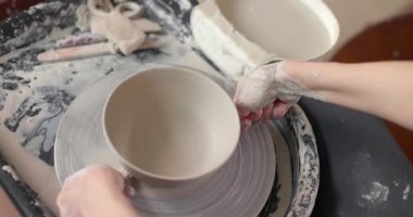 Kadın çömlekçi çömlekçi, çömlekçi çarkının ipiyle kilden bir tencereyi kesti. Yakın çekim, yavaş çekim.