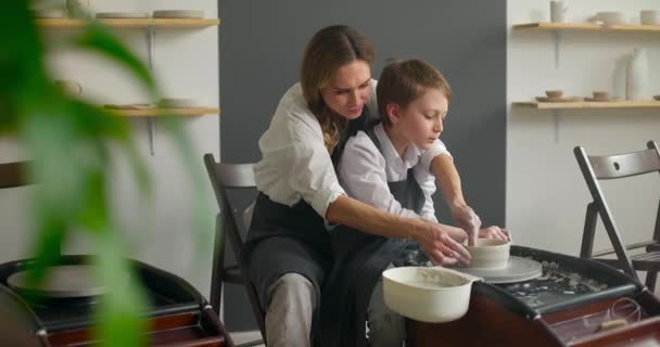 Gelukkige jonge vrouw en schattig kind jongen het maken van aardewerk op spinnen aardewerk wiel in de werkplaats. Langzame beweging — Stockvideo