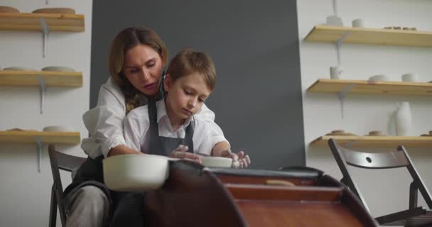 Taller de cerámica. Madre enseña a su hijo a trabajar en una rueda giratoria de cerámica. Hobby, ocio, arte y artesanía concepto. Movimiento lento — Vídeos de Stock