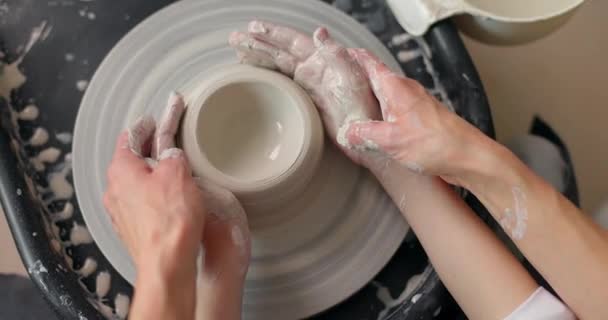 Mãos de um menino que esculpe louças de barro em uma roda de oleiros com a ajuda de sua mãe. Movimento lento — Vídeo de Stock