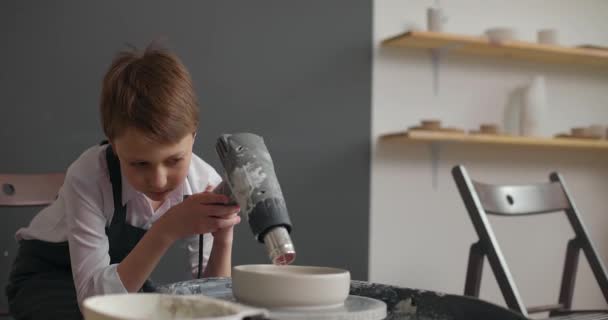 Bambino in grembiule sta asciugando vuoto ceramica su ruota rotante in studio di ceramica. Rallentatore — Video Stock