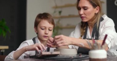 Anne ve oğul kil bir kaseyi harflerle süsler. Çömlek atölyesinde yüksek lisans. Yavaş çekim