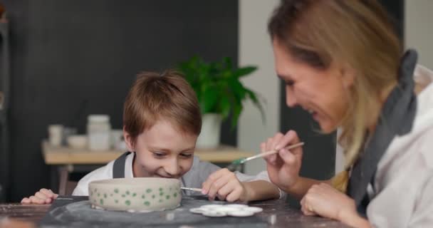 Taller de clase de cerámica. Madre enseña a su hijo feliz dibujando en un tazón de barro en un estudio de cerámica. Pasando tiempo juntos. Hobby, ocio. Movimiento lento — Vídeo de stock