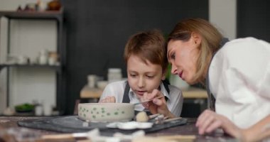 Anne, stüdyo boyama kabında oğluna yardım ediyor. Çömlek sınıfı atölyesi. Anne ve çocuk birlikte yaratıcı işler yaparak vakit geçiriyorlar. Yavaş çekim