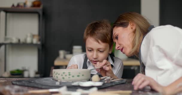 Mutter hilft ihrem Sohn beim Malen im Atelier. Töpferkurs. Mutter und Kind verbringen Zeit miteinander, um kreativ zu arbeiten. Zeitlupe — Stockvideo