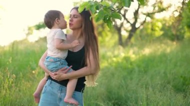 Küçük oğlu parkta kollarında mutlu bir anne. Genç anne ve tatlı bebeği eğleniyor, bebeği öpüyor. Mutlu gülümseyen insanlar. Yavaş çekim