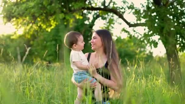 快乐的母亲和她的小儿子在公园里拥抱和旋转。年轻的妈妈和她的小儿子在一个绿色的公园里玩得很开心。笑得开心的人慢动作 — 图库视频影像