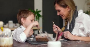 Anne ve oğlu çömlek atölyesinde, atölyede birlikte kilden bir kase çiziyorlar. Kadın çömlekçi çocuğa toprak eşyalar üzerinde resim yapmayı öğretiyor. Yavaş çekim