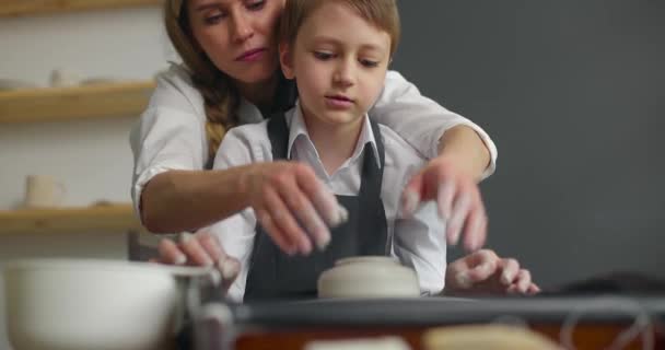 在陶瓷轮上做陶瓷壶的母亲和儿子的前视图。陶器作坊慢动作. — 图库视频影像