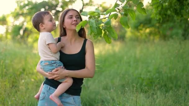 Ευτυχισμένη μητέρα με τον μικρό της χαμογελαστό γιο στην αγκαλιά της στον κήπο. Η νεαρή μαμά και το χαριτωμένο μωρό της διασκεδάζουν. Αργή κίνηση — Αρχείο Βίντεο