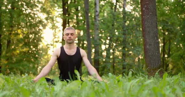 A fiatalember a gyepen meditál a Városligetben. A lótuszban üldögélő férfiak napkeltekor a szabadban meditálnak. Lassú mozgás. — Stock videók