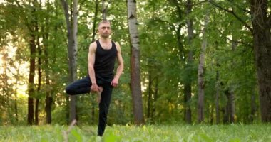 Güneşli yaz gününde erkekler parkta yoga ve meditasyon yapıyor. Tek ayak üstünde denge. Yavaş çekim