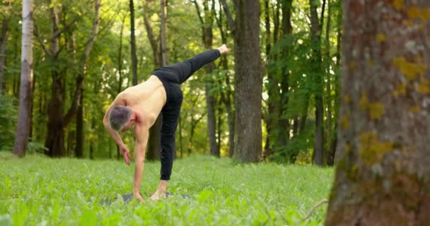 Uomo che fa yoga asana sull'erba in città park.Yogi esecuzione di equilibrio in piedi una gamba al mattino — Video Stock