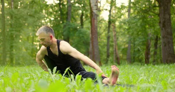 Мужчина занимается йогой в красивом парке. Спортсмен перемещает вес с одной ноги на другую, балансируя на траве. — стоковое видео