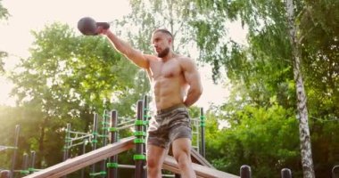 Açık havada egzersiz yapan bir adam. Şehir parkında bir koluyla kettlebell ağırlığını kaldıran bir adam.