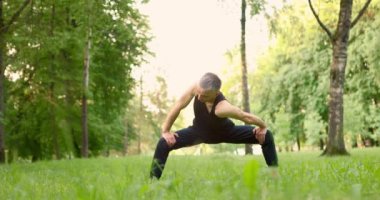 Sabahları yoga yapan genç bir adam parkta poz veriyor. Adam esneme hareketleri yapıyor. Yavaş çekim