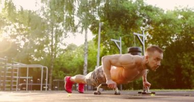 Athletic man holding metal handles and doing classical push-ups on sports ground on sunny day