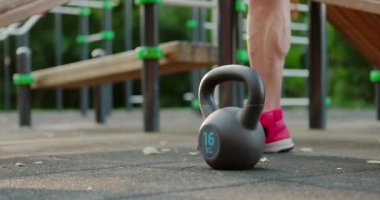 Spor sahasında kettlebell kaldıran bir adam. Şehir parkında yoğun egzersizler yapan bir sporcu.
