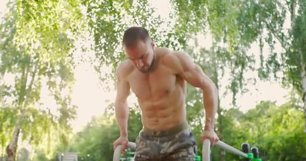 Hübscher Bodybuilder turnt allein am parallelen Barren. Mann macht Liegestütze auf Sportplatz — Stockvideo