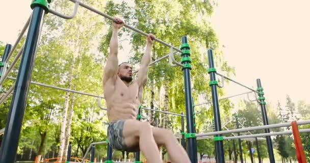 Joven hombre musculoso colgando en la barra horizontal y levantando las piernas.Atleta construcción de músculos abdominales — Vídeo de stock